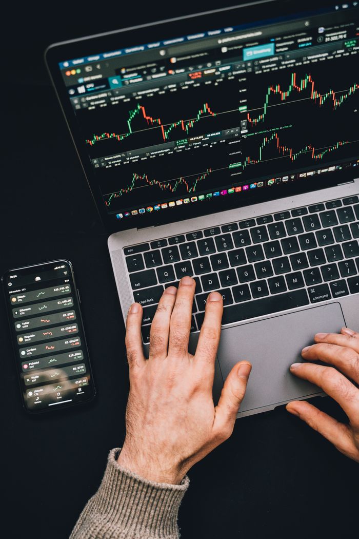 project-01-b Hands typing on a laptop with cryptocurrency charts and smartphone display in view, focusing on digital finance.